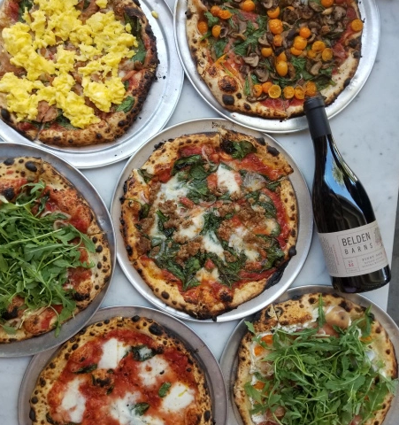 Photo of several pizzas and a bottle of red wine